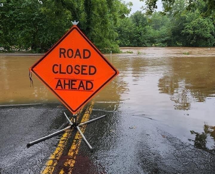 Road closed ahead sign sits in the middle of a flooded road